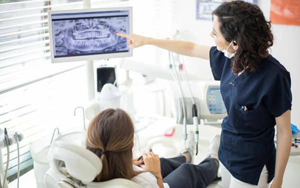 Dental hygienist pointing at X-ray image while consulting with patient in modern dental office.