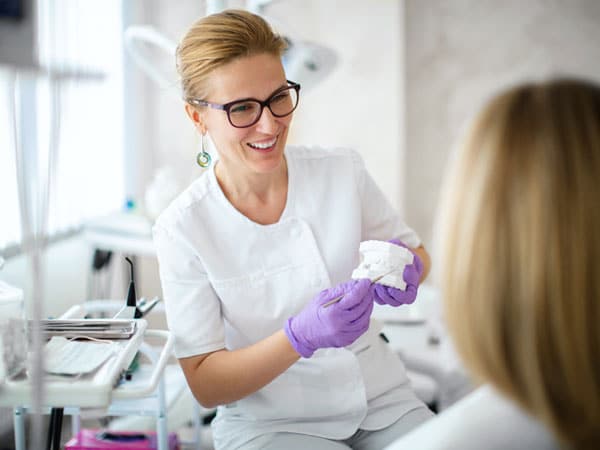 Dental professional in white uniform and purple gloves holding sample during patient consultation in modern dental office.