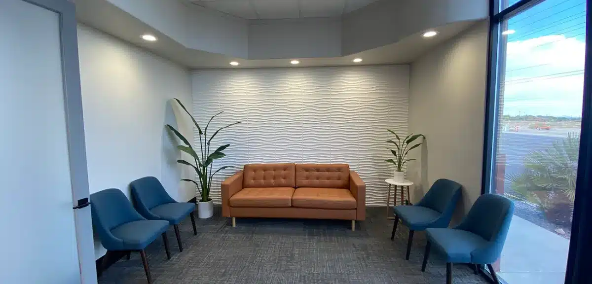 Modern dental waiting room with orange sofa and blue chairs against white brick wall.