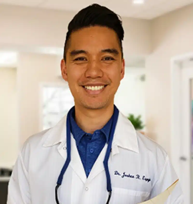 Young male dentist in white coat and stethoscope smiling in modern dental office.